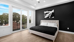 A bedroom with a large bed, a ceiling fan, and a view through a sliding glass door to an outdoor balcony. - Newly Built Modern 3 Bedroom Houston Home (Houston)