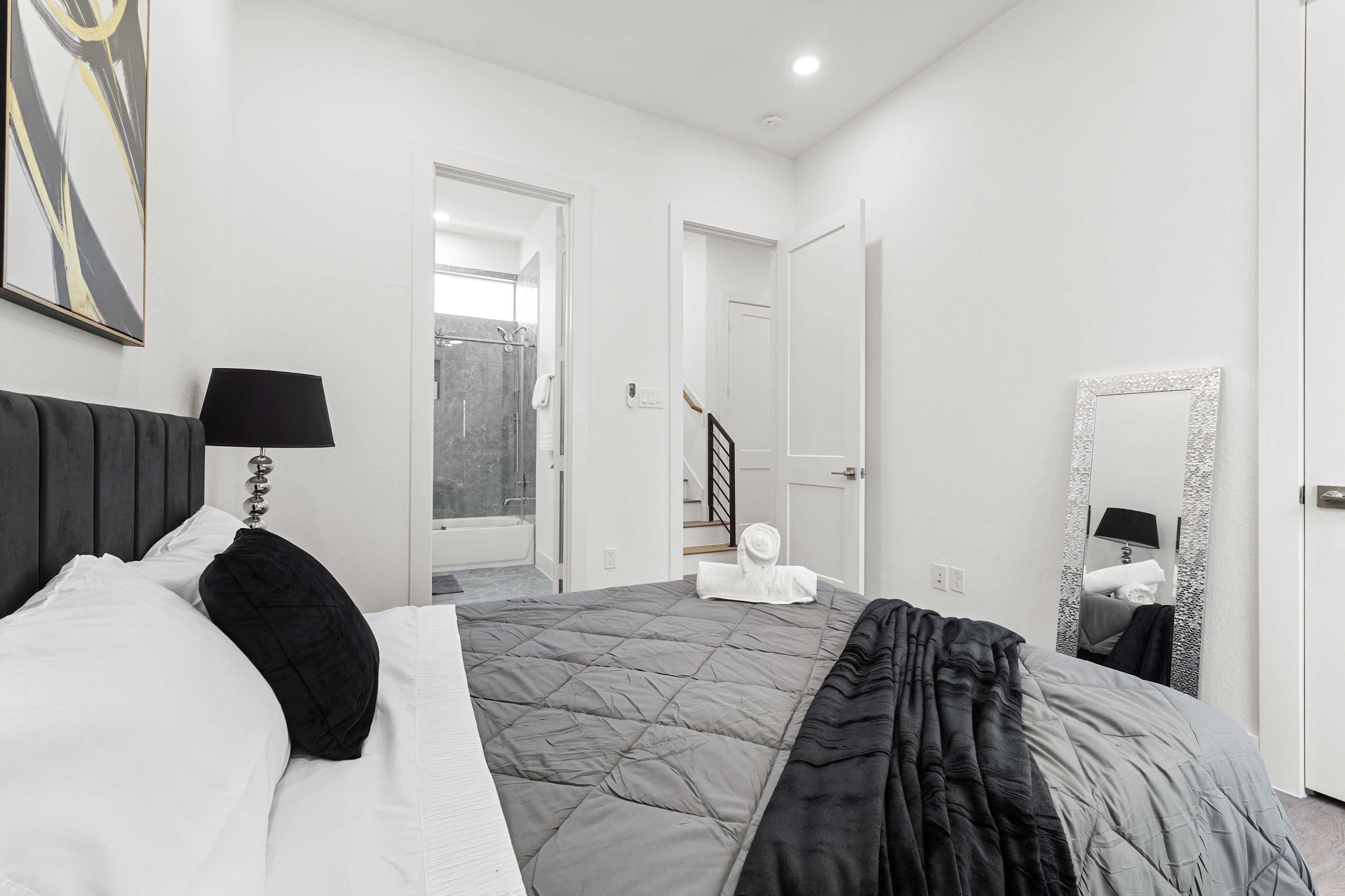 Une chambre à coucher comprenant un lit, une lampe de chevet, un miroir et une porte donnant sur une salle de bain.