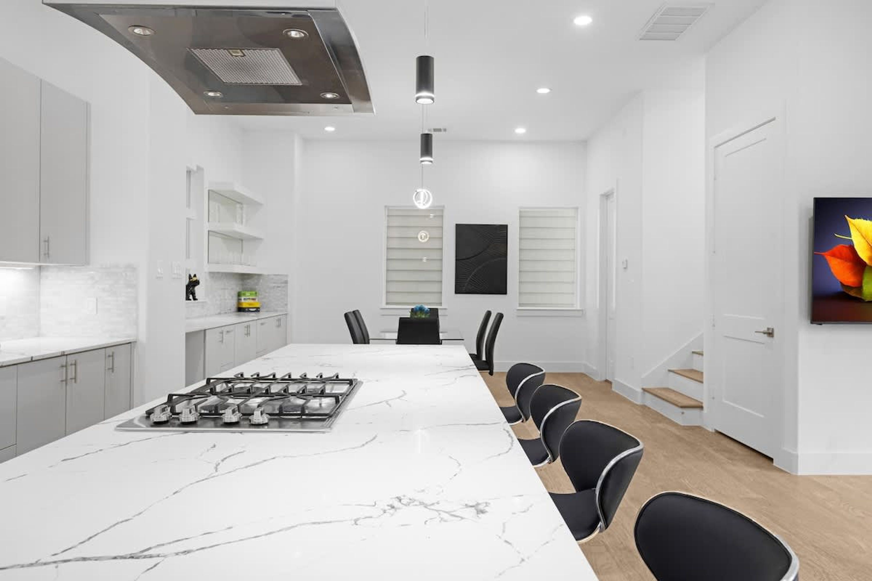 A modern kitchen with a large island, white cabinetry, and a dining area with chairs.