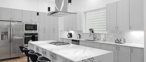 A modern kitchen with a marble island, stainless steel appliances, and black bar stools.