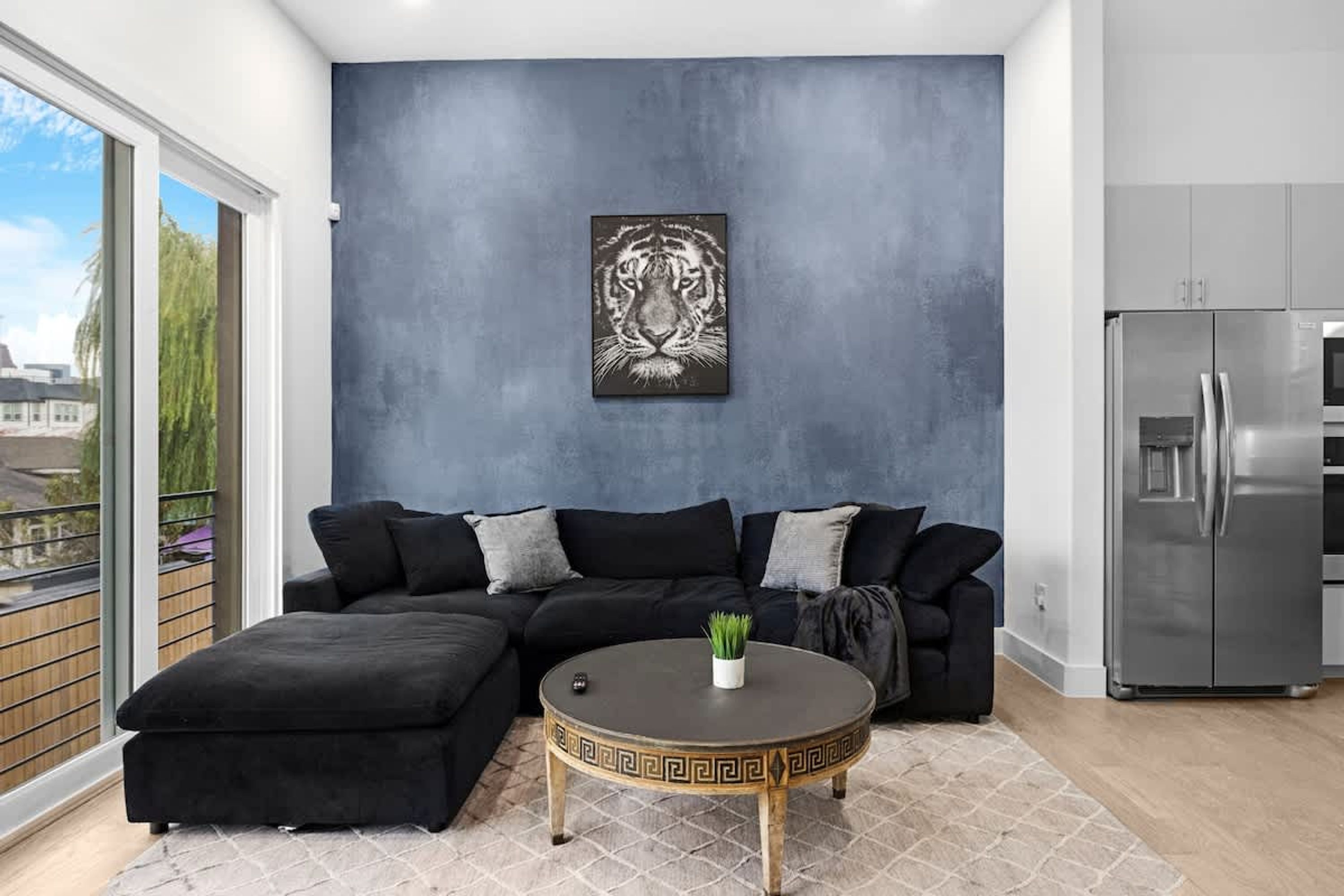 A modern living room with a sectional sofa, a round coffee table, and a large window offering a view of buildings and trees.
