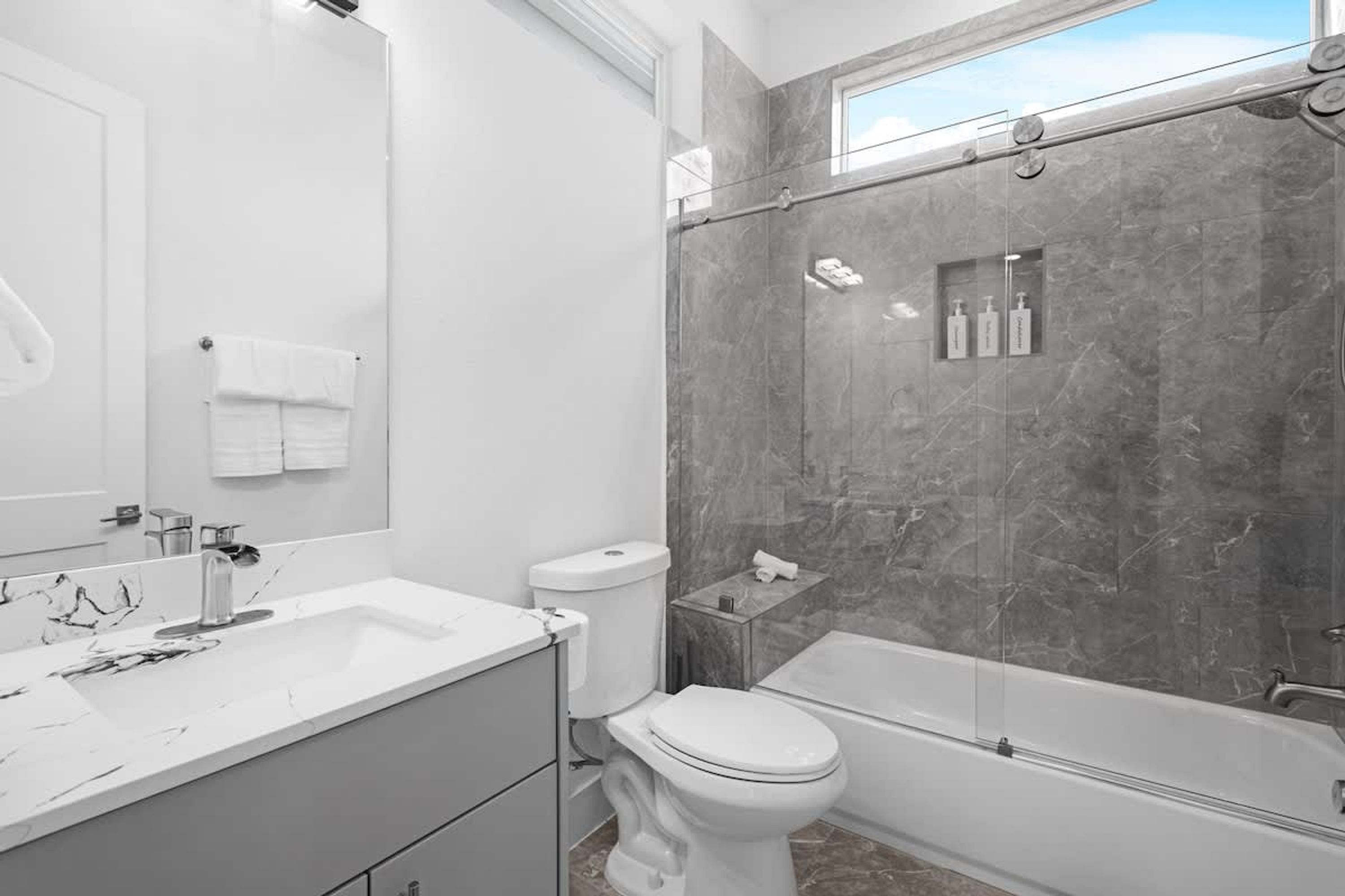 A modern bathroom with a marble shower, a white toilet, and a large mirror.