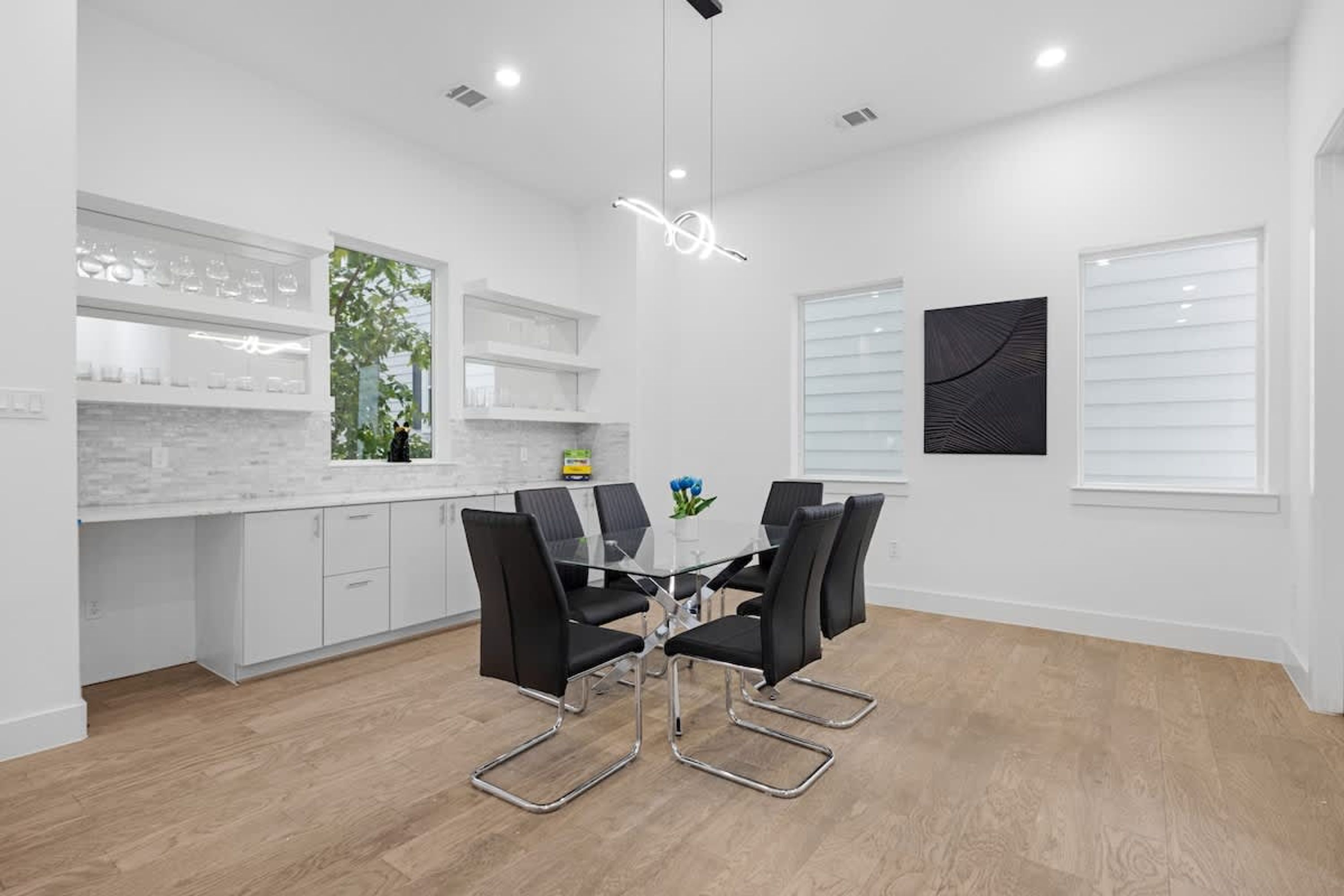 A modern kitchen with white cabinetry, a glass dining table, and black chairs.