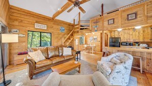 A cozy cabin interior with a wooden interior, a dining area, a kitchen, and a staircase leading to a loft.
