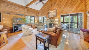 A spacious wooden cabin interior with a fireplace, leather seating, and large windows.