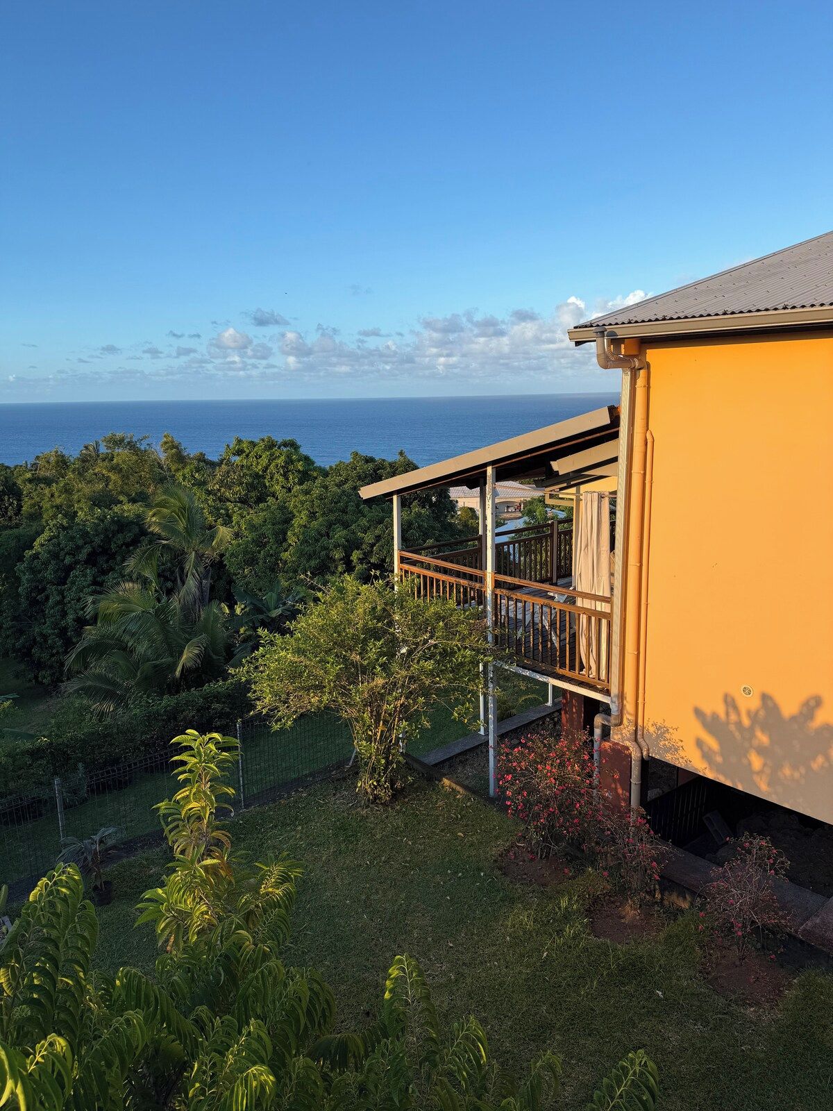 A yellow building with a balcony overlooking a lush green landscape and the ocean.