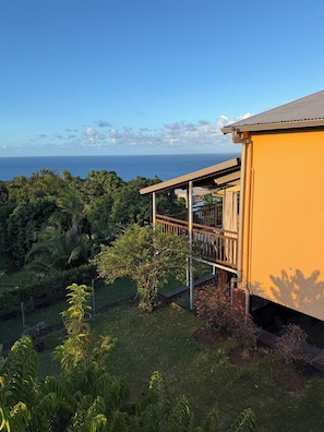 A yellow building with a balcony overlooking a lush green landscape and the ocean.