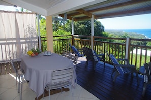 A covered outdoor dining area with a table and chairs, overlooking a scenic landscape.