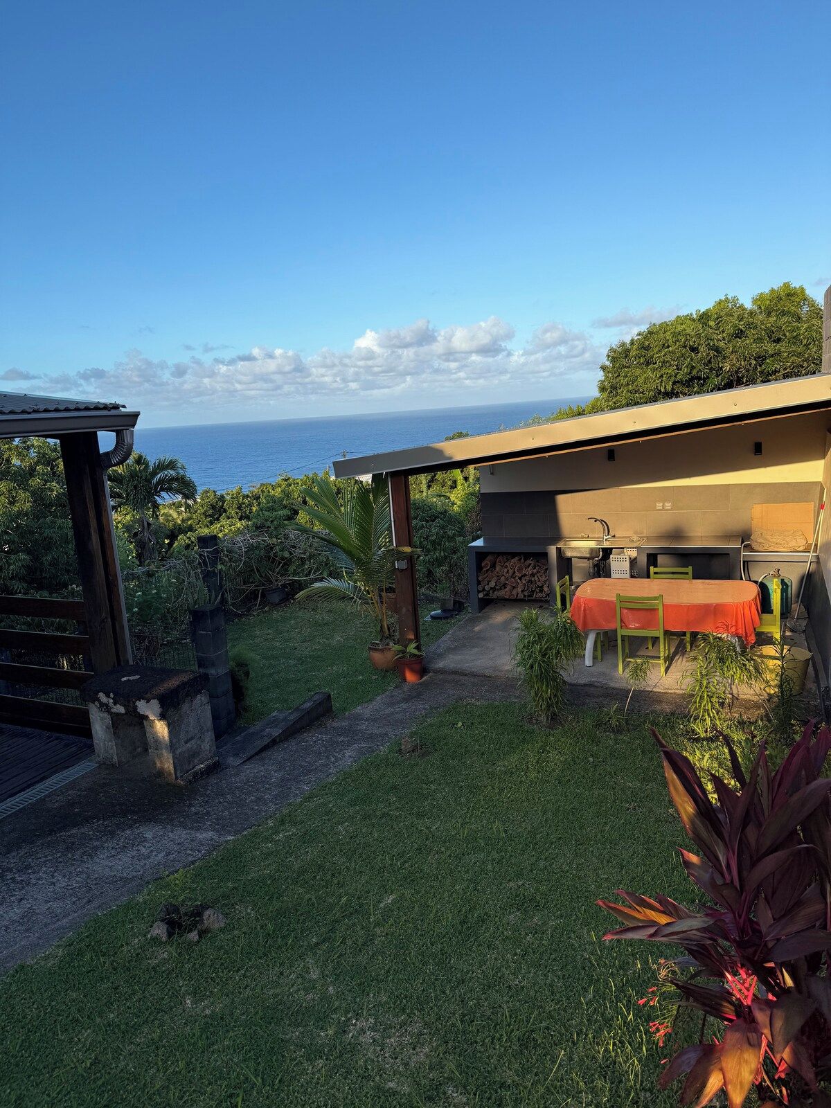 A modern outdoor area with a dining table and chairs, a small kitchen area, and a view of the ocean.