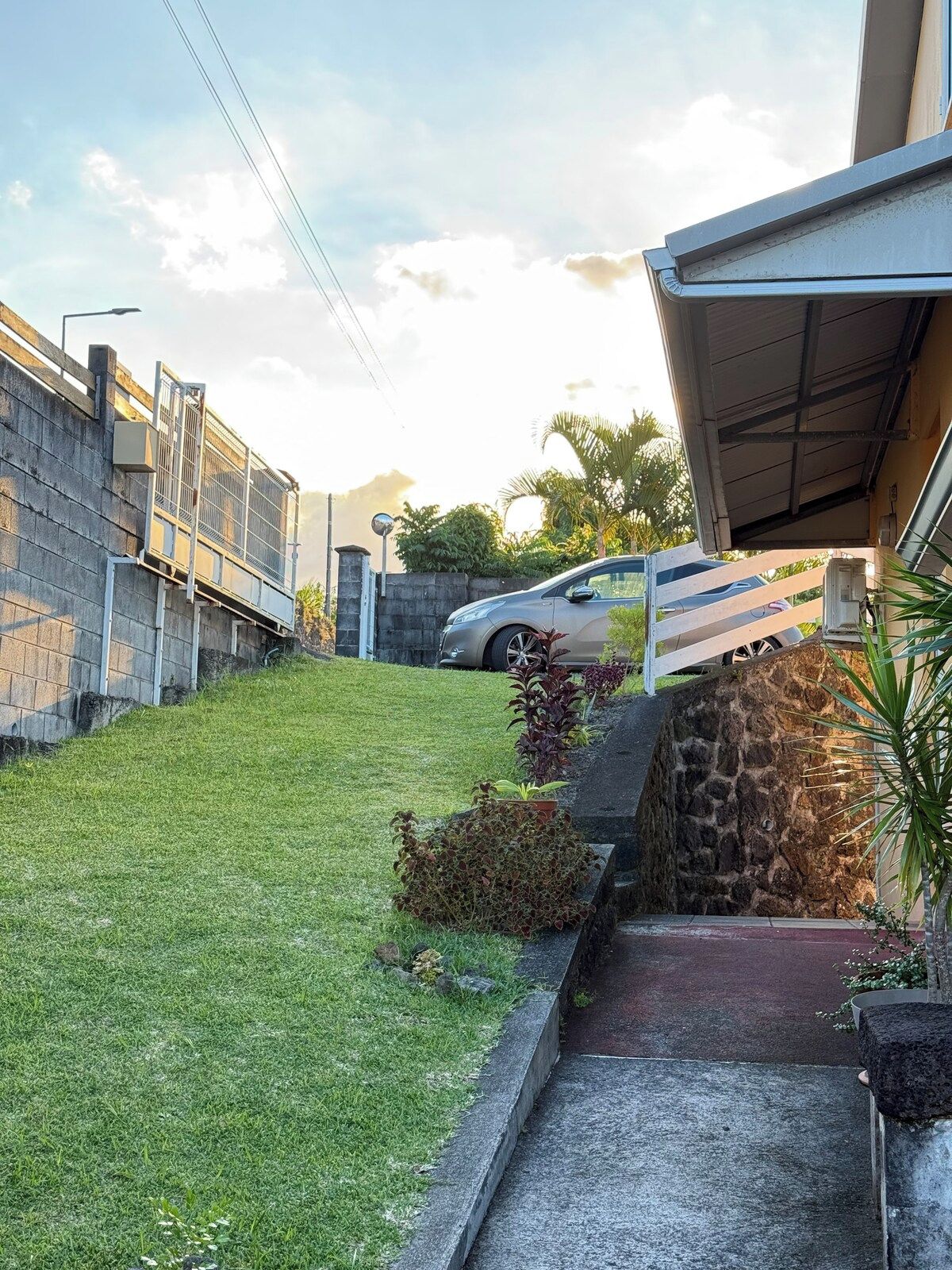 Una propiedad residencial con entrada en cuesta, un coche estacionado y un muro de piedra.