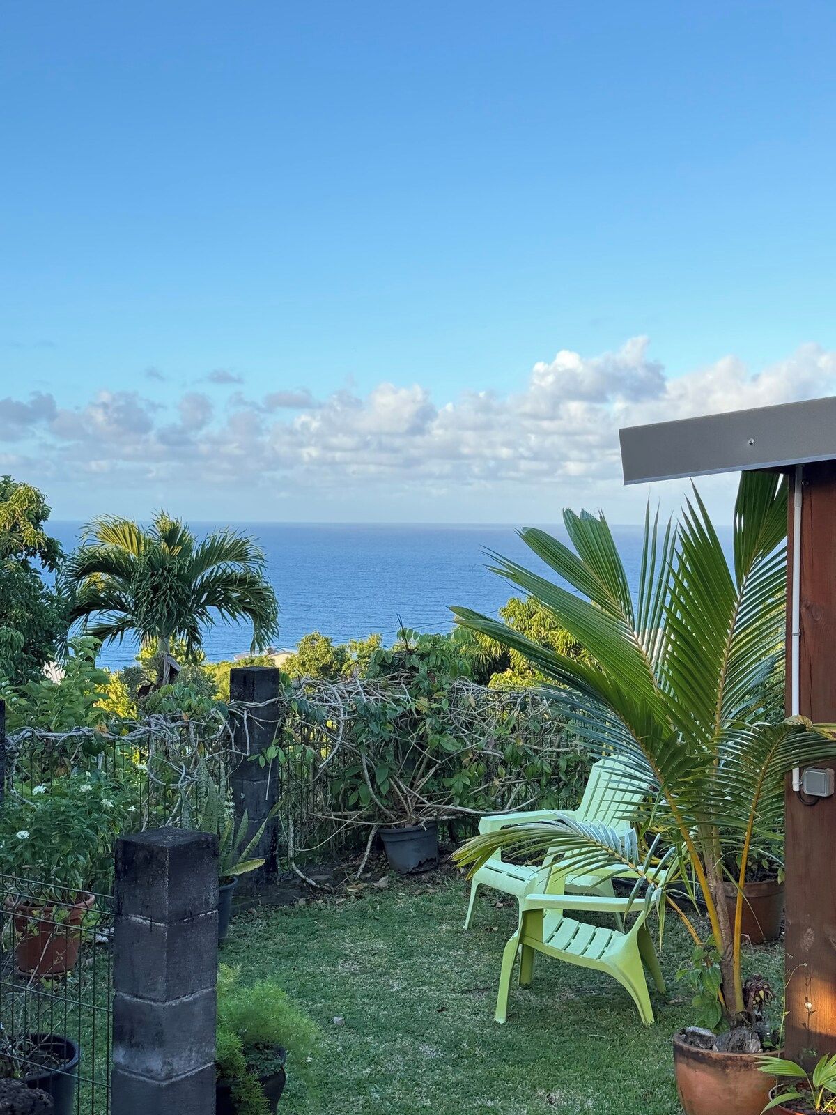 A patio with a view of the ocean, green chairs, and potted plants.