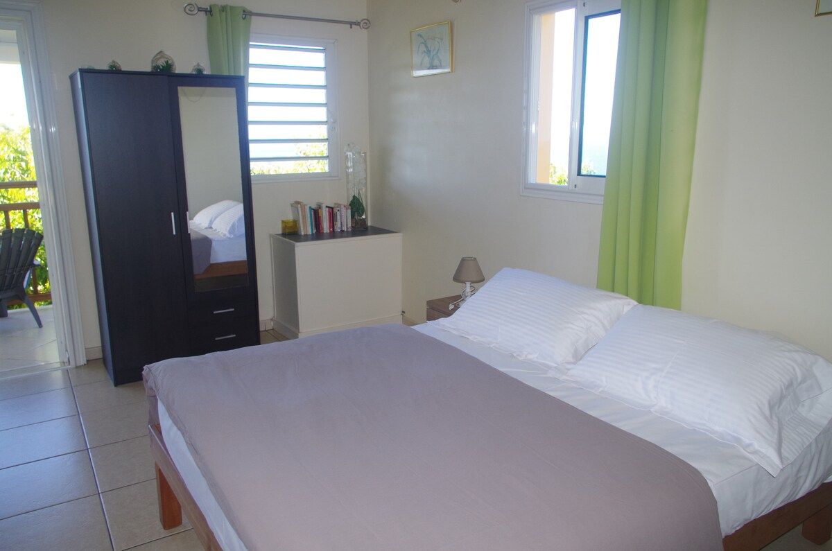 A bedroom with a bed, a wardrobe, a nightstand, a lamp, and a window with curtains.