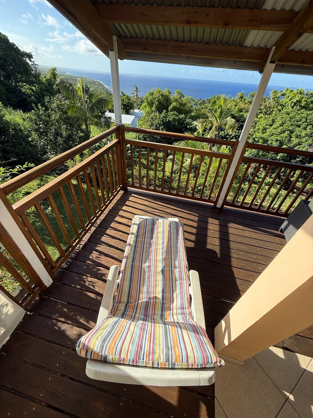 A wooden deck with a single lounge chair and a colorful striped cushion.