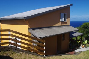 Een gebouw met twee verdiepingen, een balkon, een houten omheining en uitzicht op de oceaan.