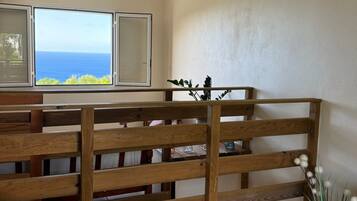 A room with a view of the ocean, a wooden partition, a table with a floral tablecloth, and a vase with white flowers.