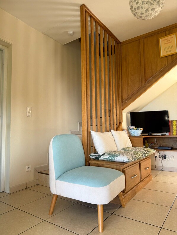 A room with a wooden partition, a television, a sofa with patterned cushions, and a cabinet with drawers.