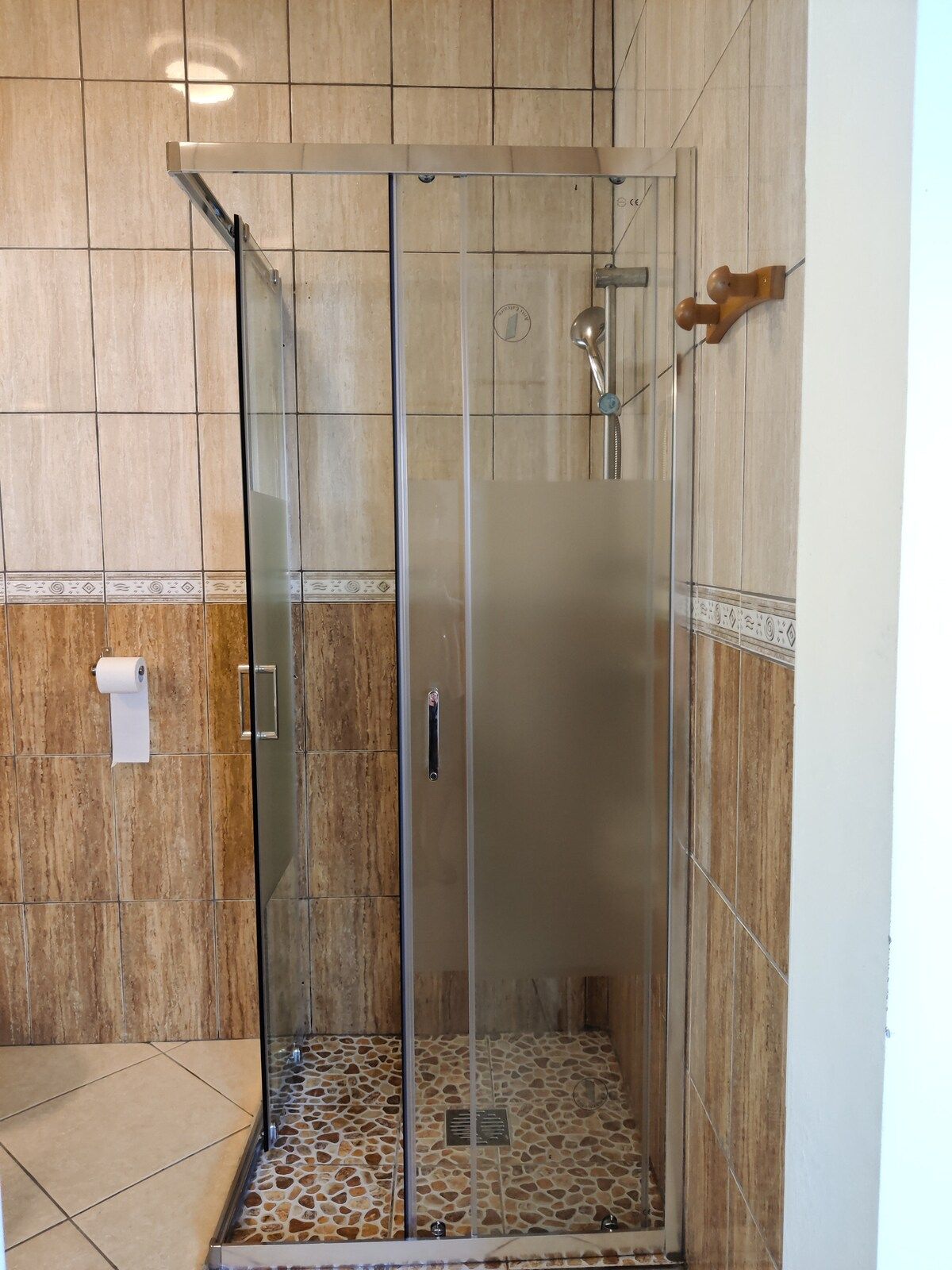 A glass-enclosed shower stall with a tiled floor and wooden wall panels.