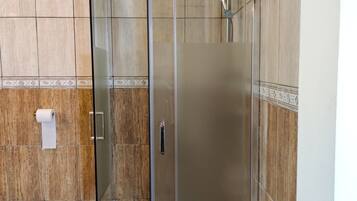 A glass-enclosed shower stall with a tiled floor and wooden wall panels.