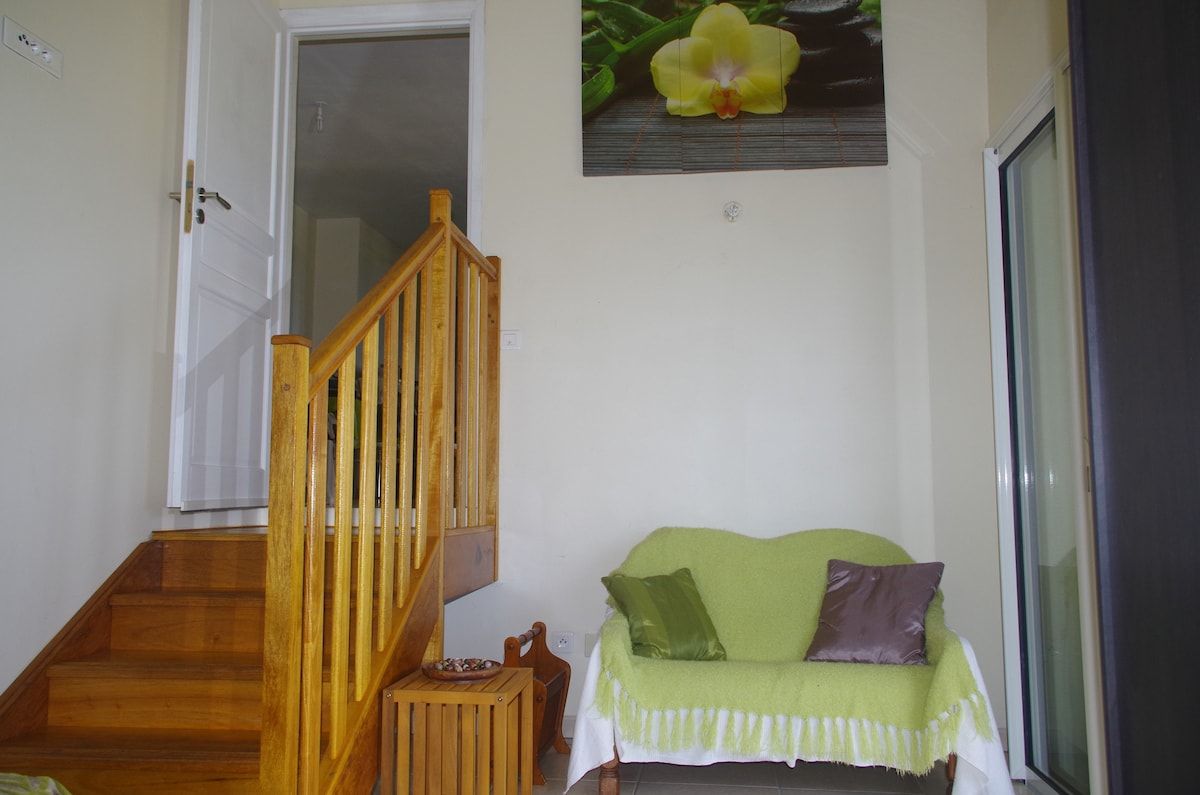 A staircase leading to a room with a green sofa and a flower painting on the wall.