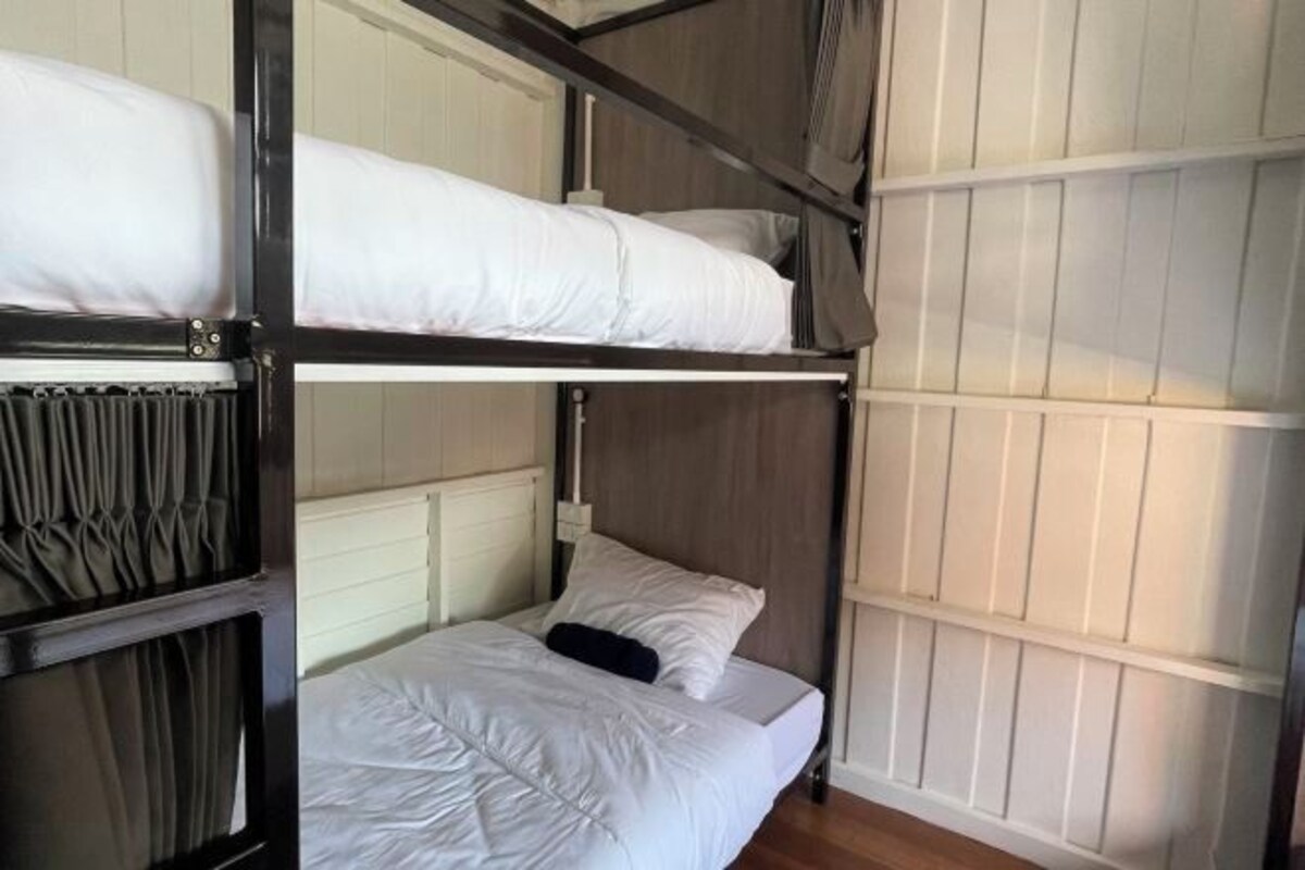 Quarto com beliche, cabeceira de madeira, roupa de cama branca e painéis brancos na parede.