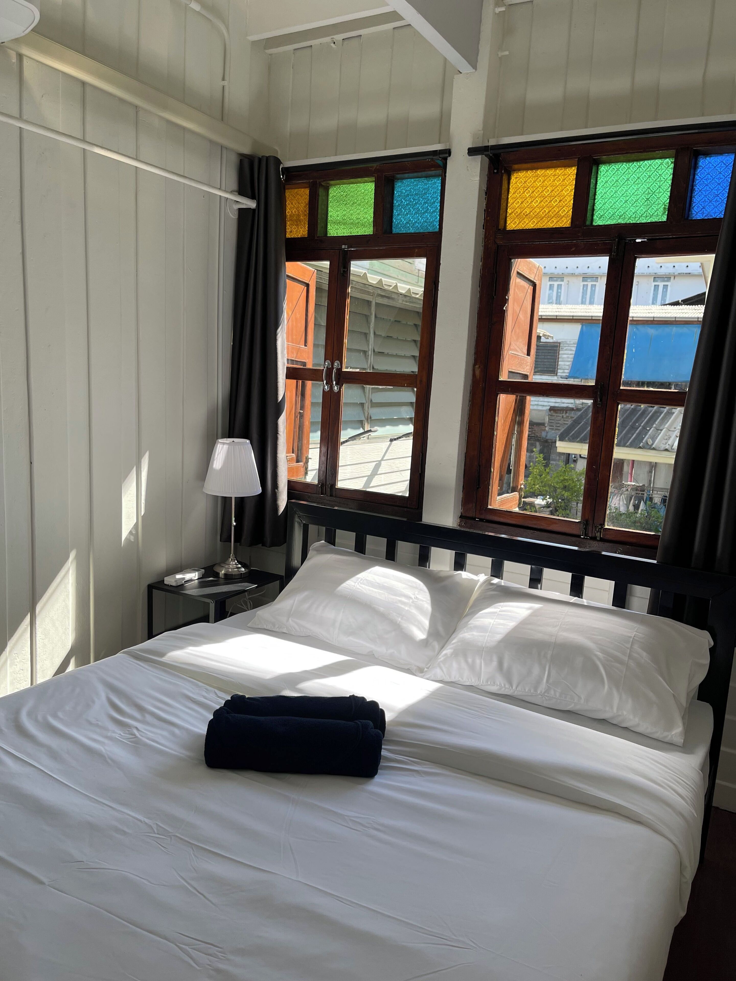 A hotel room with a bed, a nightstand, a lamp, and a window with colorful panes.