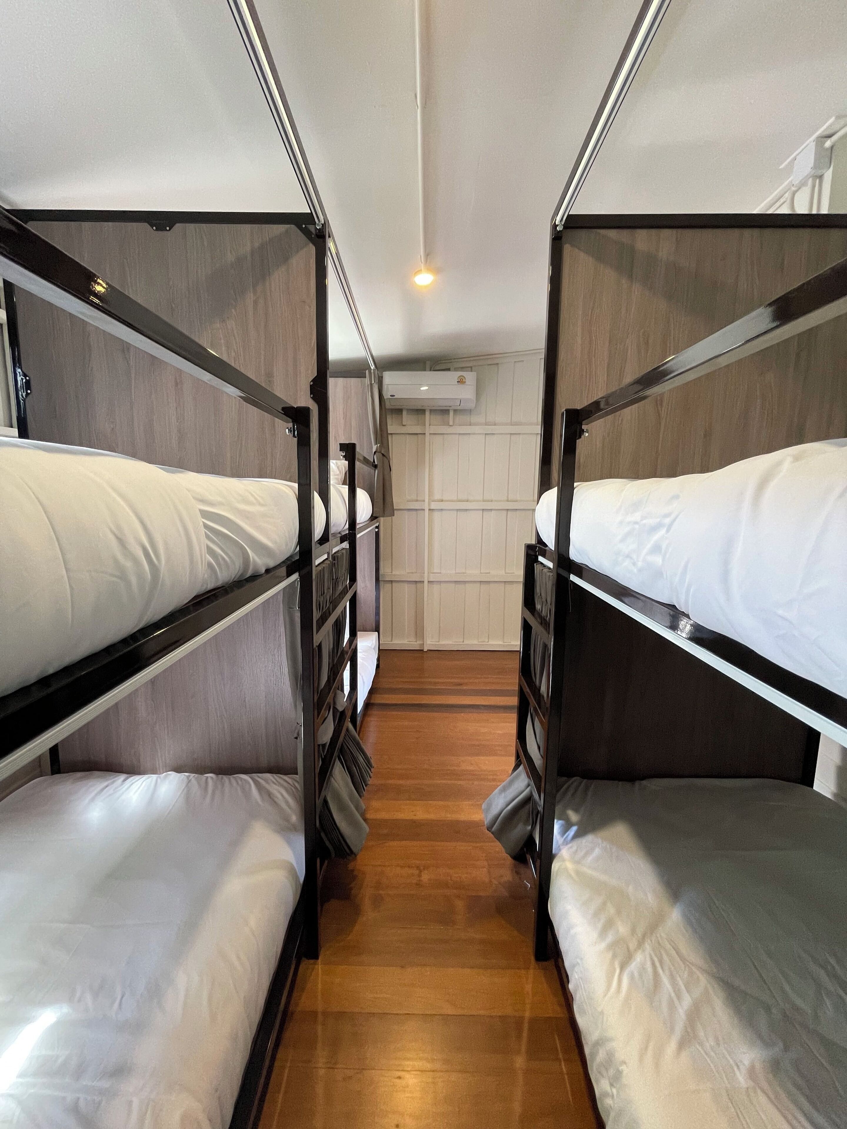 A corridor with bunk beds, wooden flooring, and an air conditioning unit on the wall.