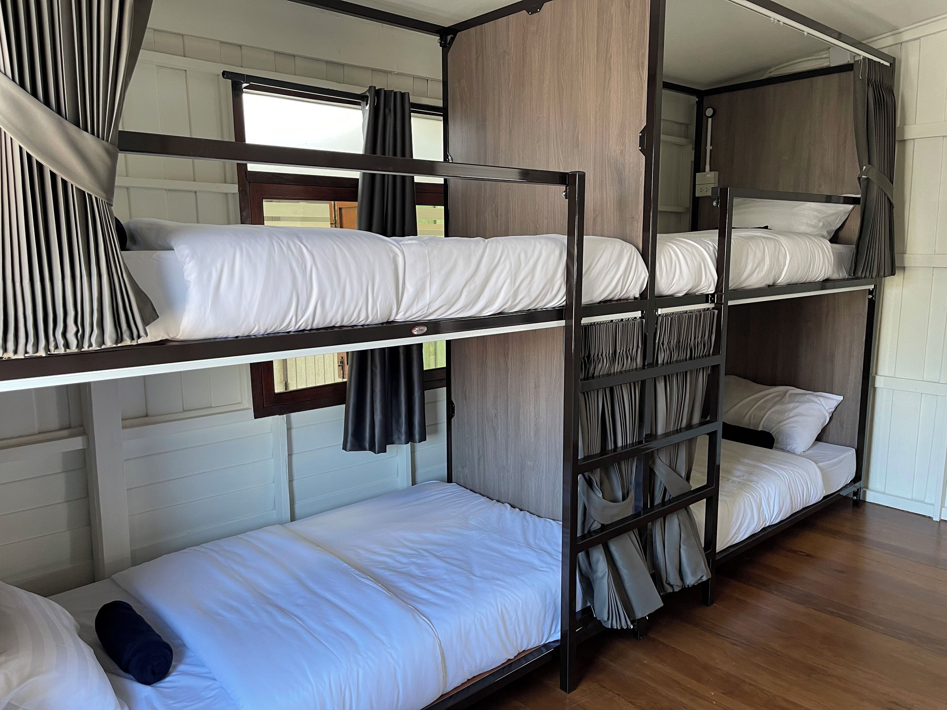 A bunk bed room with wooden headboards, white bedding, and curtains.