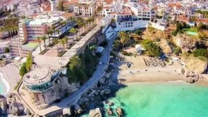 Luftaufnahme einer Küstenstadt mit einem markanten Strand, felsiger Küstenlinie und einer Mischung aus Wohn- und Geschäftsgebäuden.
