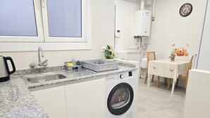 Ett kompakt kök med en inbyggd tvättmaskin, ett handfat och en matplats med ett bord och stolar.