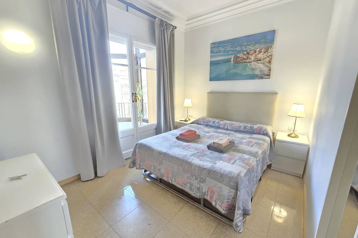 A hotel room with a bed, two bedside lamps, a painting on the wall, and a window with curtains.