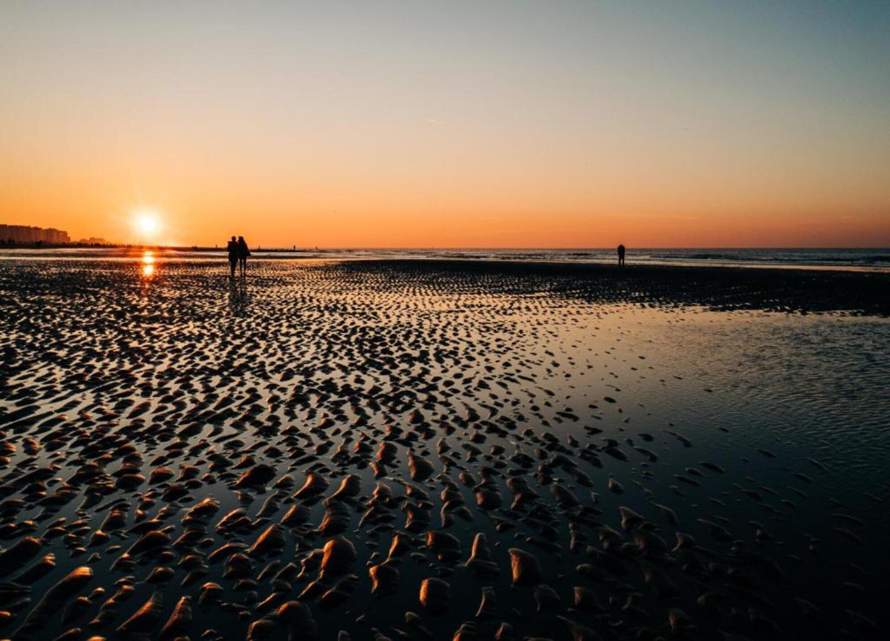 Spiaggia al tramonto con impronte sulla sabbia e sagome di persone.