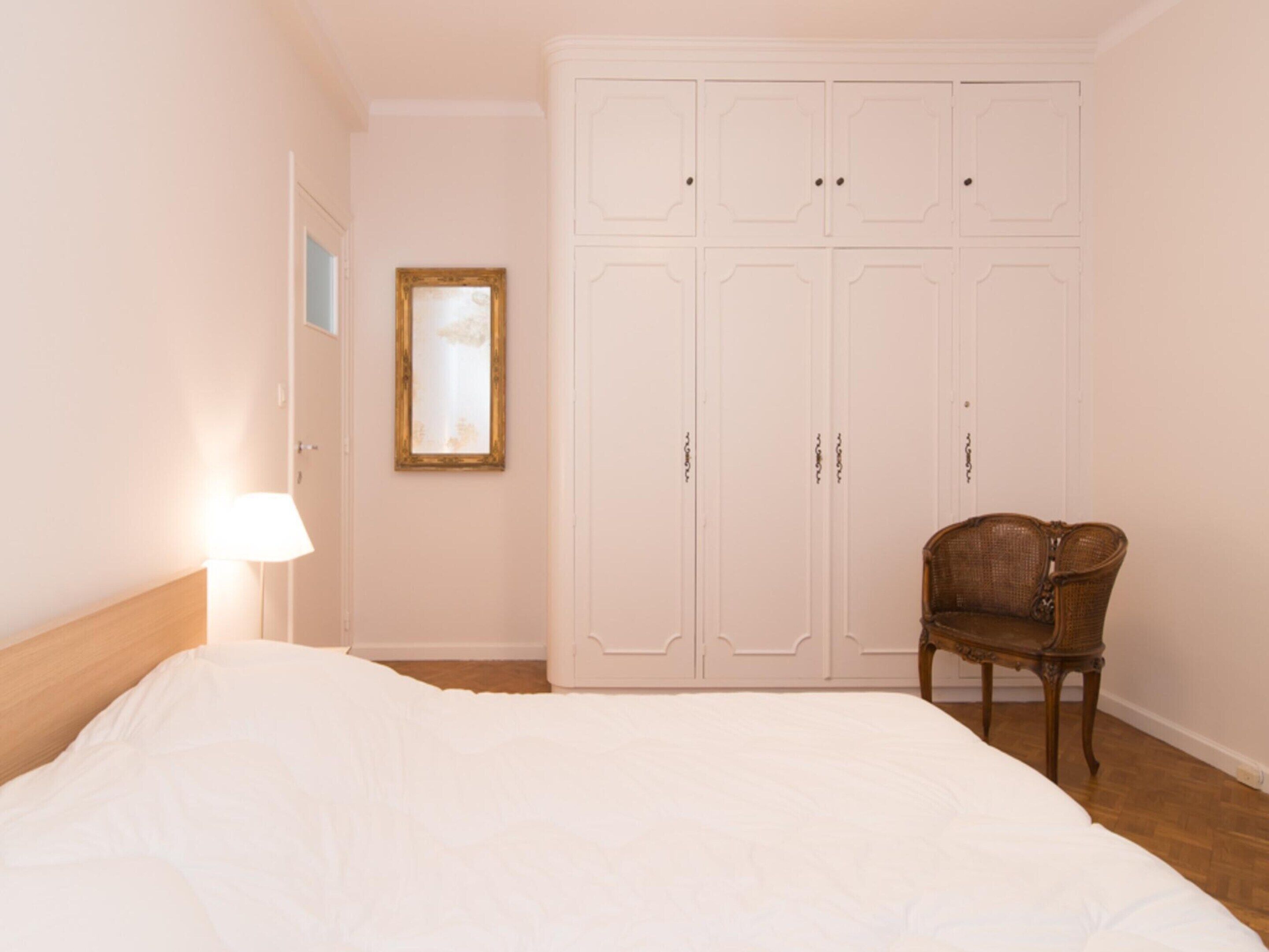 A bedroom with a bed, a wardrobe, a chair, and a lamp.