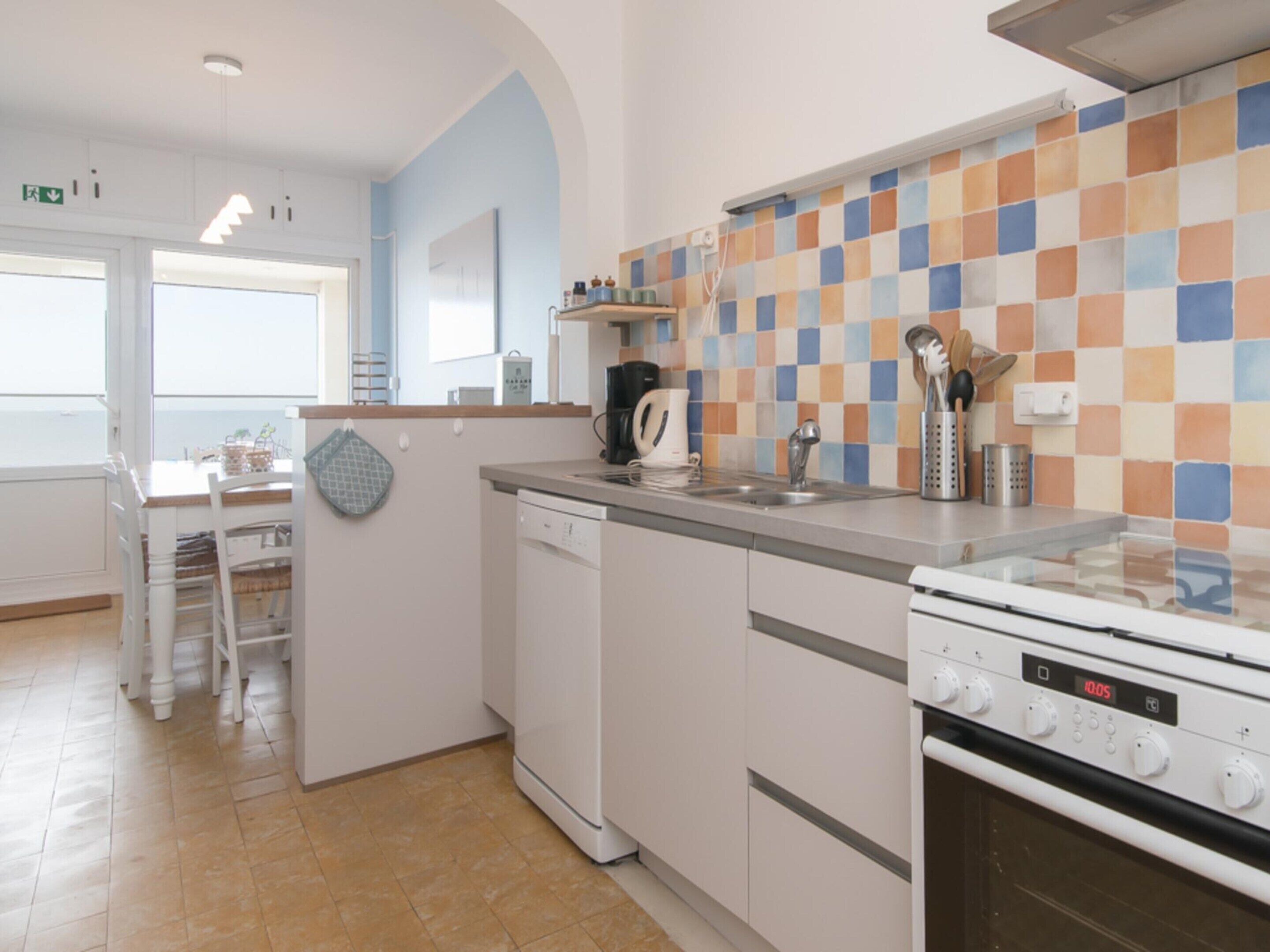 A kitchen with a tiled backsplash, a dishwasher, a stove, and a sink.