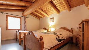 A room with two wooden beds, a wooden wardrobe, a window with curtains, and a framed picture on the wall.