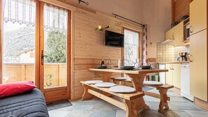 A cozy wooden cabin with a dining table set for four, a TV mounted above the table, and a kitchen area with cabinets and appliances.