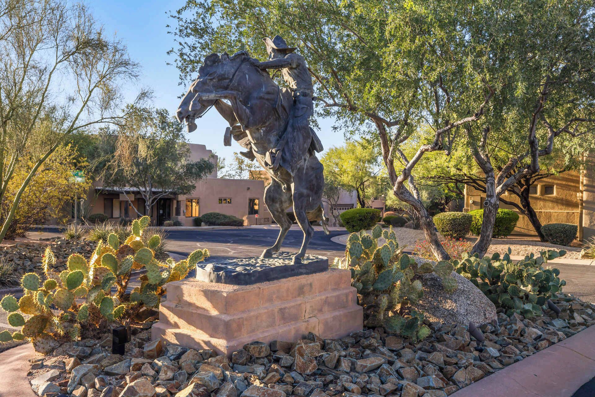 A statue of a man on a horse in a landscaped area with cacti and trees.