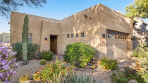 A stucco house with a garage, surrounded by a garden with cacti, succulents, and flowering plants.