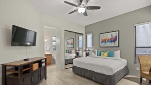 A bedroom with a large bed, a TV, a ceiling fan, and artwork on the walls.