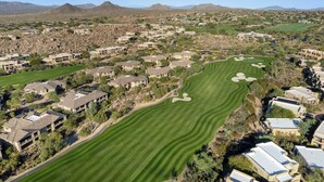 An aerial view of a golf course with residential buildings surrounding it.