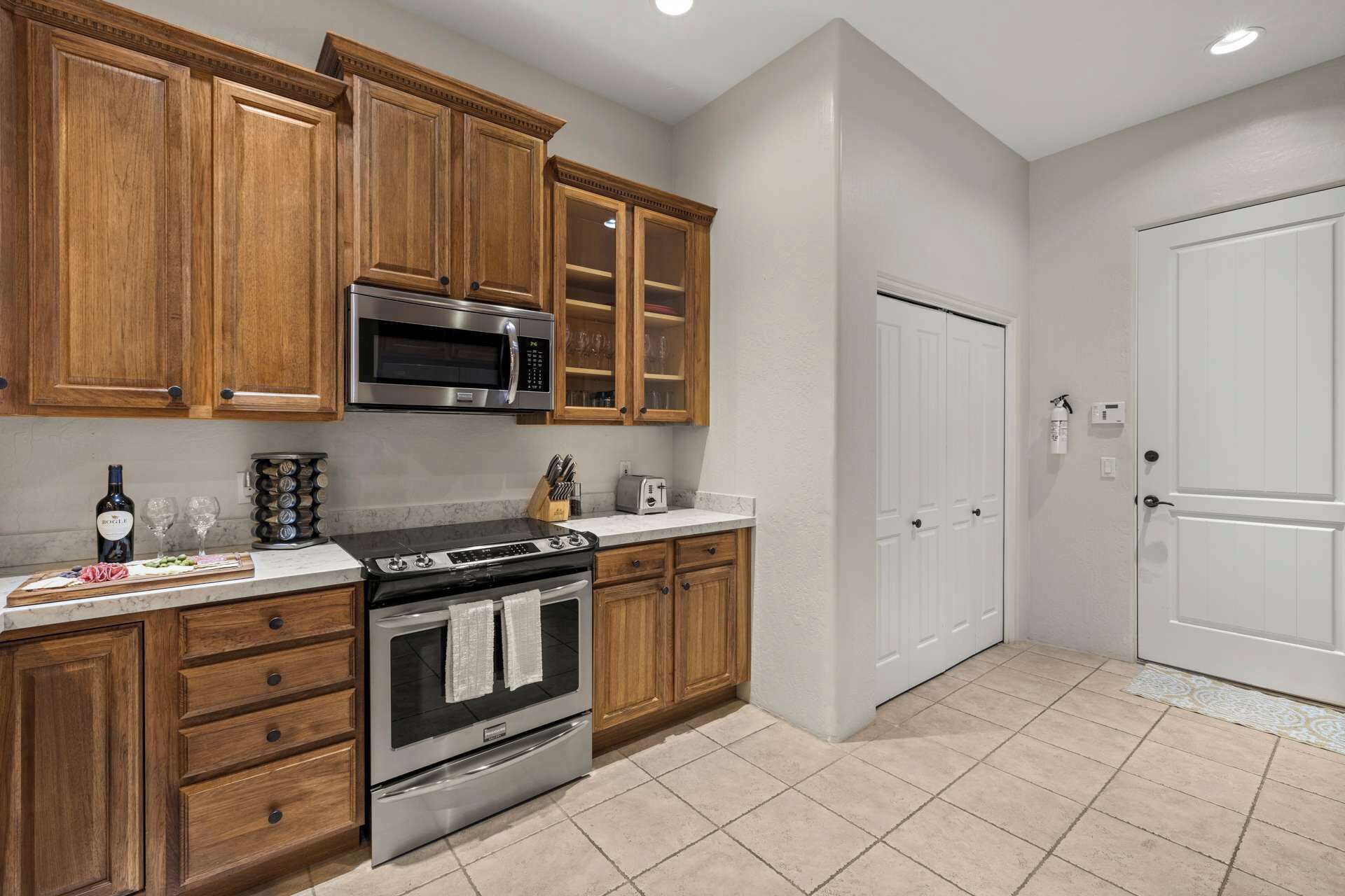 A kitchen with wooden cabinets, a stainless steel microwave, an oven, and a white door.