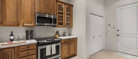 A kitchen with wooden cabinets, a stainless steel microwave, an oven, and a white door.