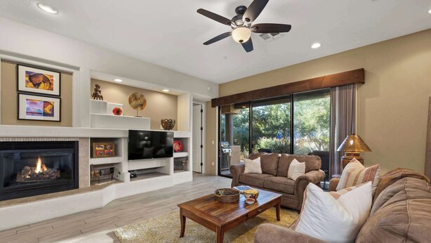 A living room with a fireplace, a ceiling fan, and a large window.