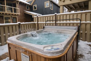 Ein Whirlpool in einem verschneiten Garten mit Holzzaun und Häusern im Hintergrund.
