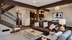 A spacious living room with a brown leather sofa, a grey sofa, a wooden coffee table, and a dining area with a chandelier. - Ski Ya Soon At Silver Star! 2 Bedroom Condo (Park City)