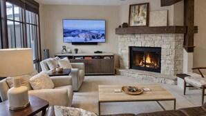 A cozy living room with a stone fireplace, a flat-screen TV mounted above it, and comfortable seating. - Ski Ya Soon At Silver Star! 2 Bedroom Condo (Park City)