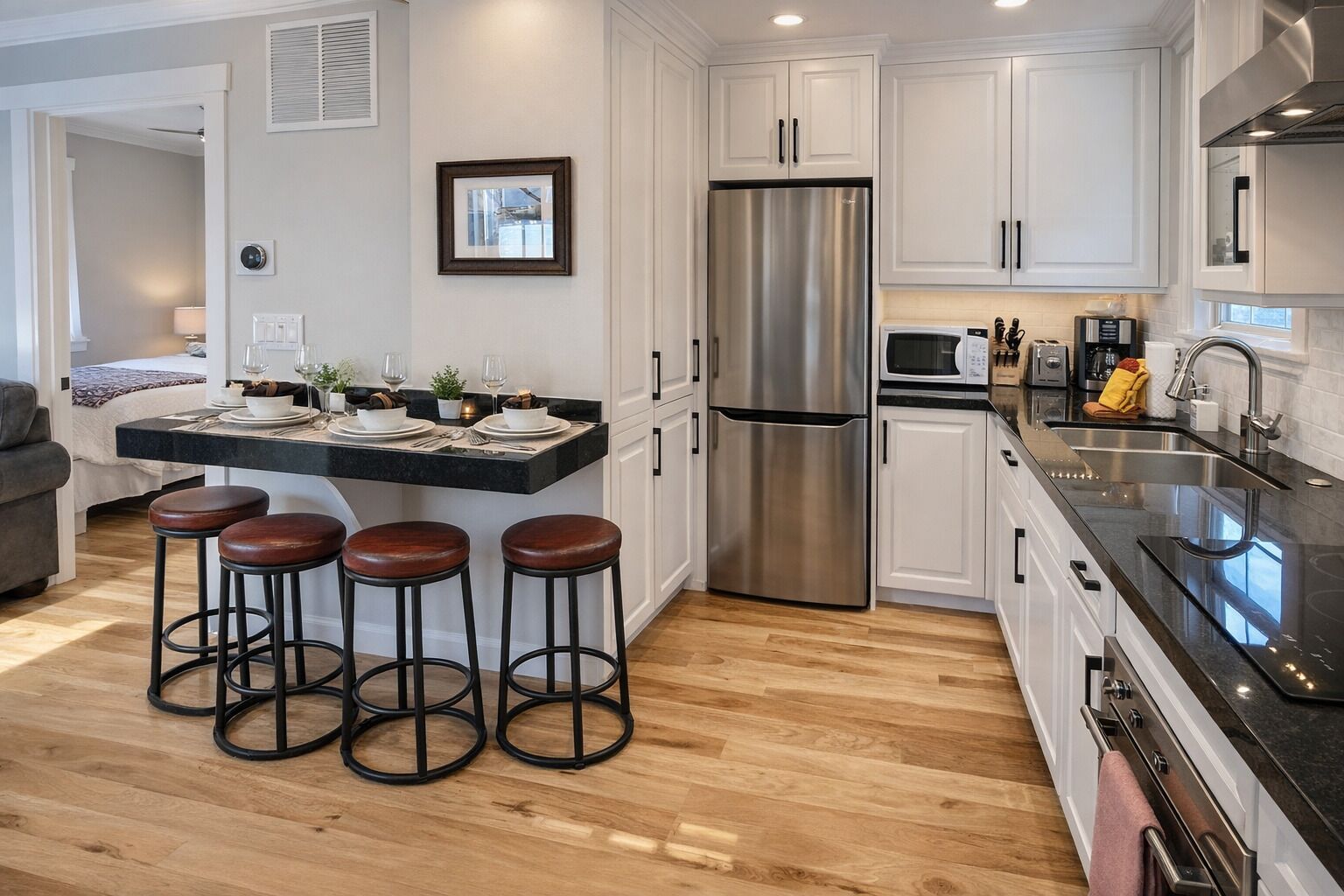A modern kitchen with a stainless steel refrigerator, white cabinets, a black countertop, and three stools.