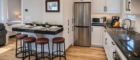A modern kitchen with a stainless steel refrigerator, white cabinets, a black countertop, and three stools.