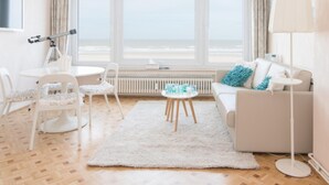 A modern living room with a large window, a white sofa, a round coffee table, and a white rug. - Frontal sea View Studio Apartment in Ostend (Ostend)