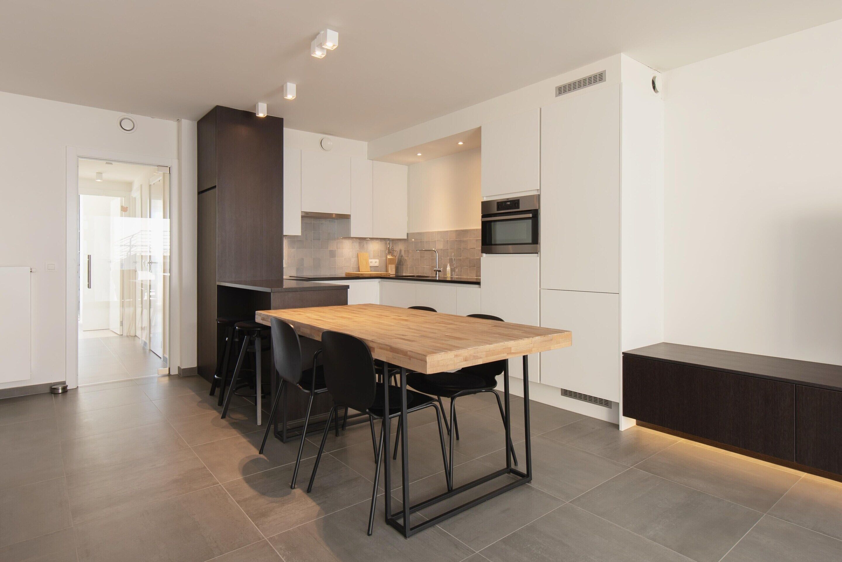 A modern kitchen with a wooden table, black chairs, and white cabinetry.
