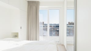 A modern hotel room with a large bed, a sliding door to a balcony, and a city view. - Apartment Close to the sea Wall of Mariakerke (Ostend)